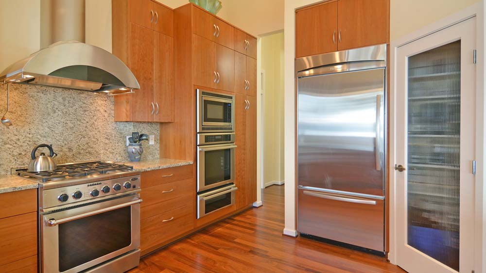 A kitchen with a stainless steel oven, vent hood & fridge